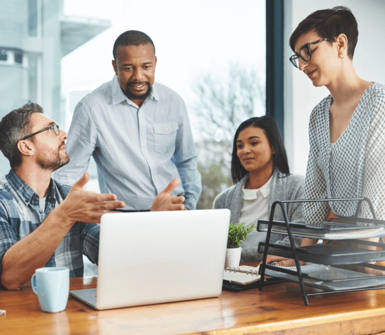 Four people gathered around a desk chatting in a businesslike manner.